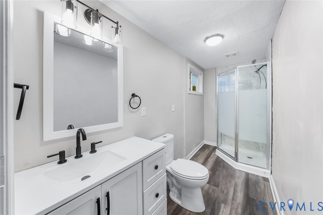 1802 Maury Street, Richmond, VA 23224 White vanity with a rectangular sink, matte black hardware, wood-finish flooring, and a glass-enclosed shower with a rainfall showerhead