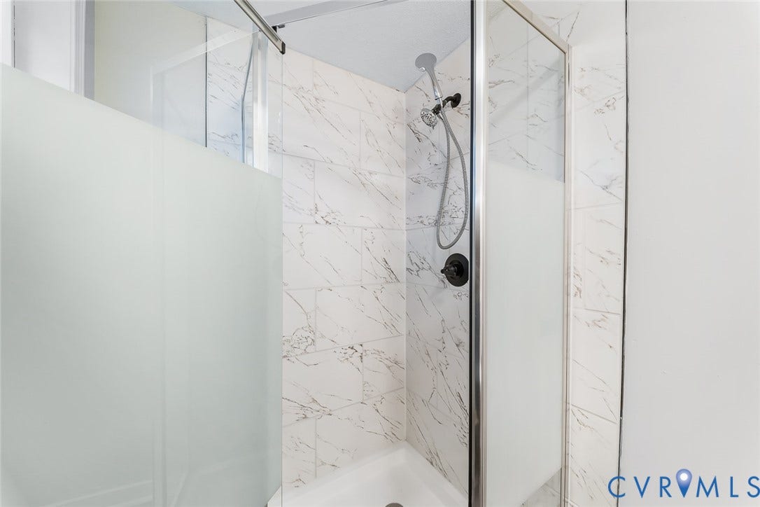 1802 Maury Street, Richmond, VA 23224 Walk-in shower enclosure featuring large-format patterned wall tile, sliding frosted glass doors, chrome frame, and a wall-mounted handheld shower fixture with dark finish hardware