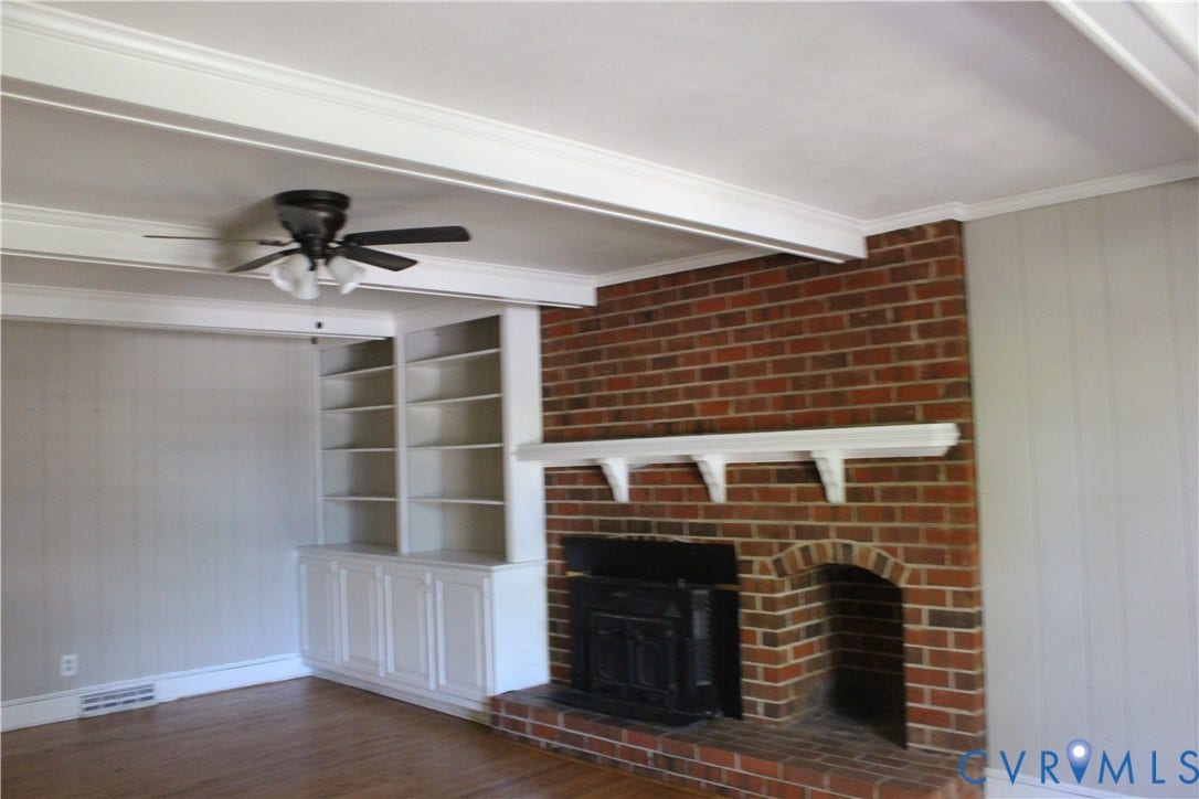 4101 Vauxhall, Chesterfield, VA 23234 Floor-to-ceiling red brick fireplace with an attached mantel, wood-finish flooring, exposed ceiling beams, and built-in white cabinetry with integrated shelving