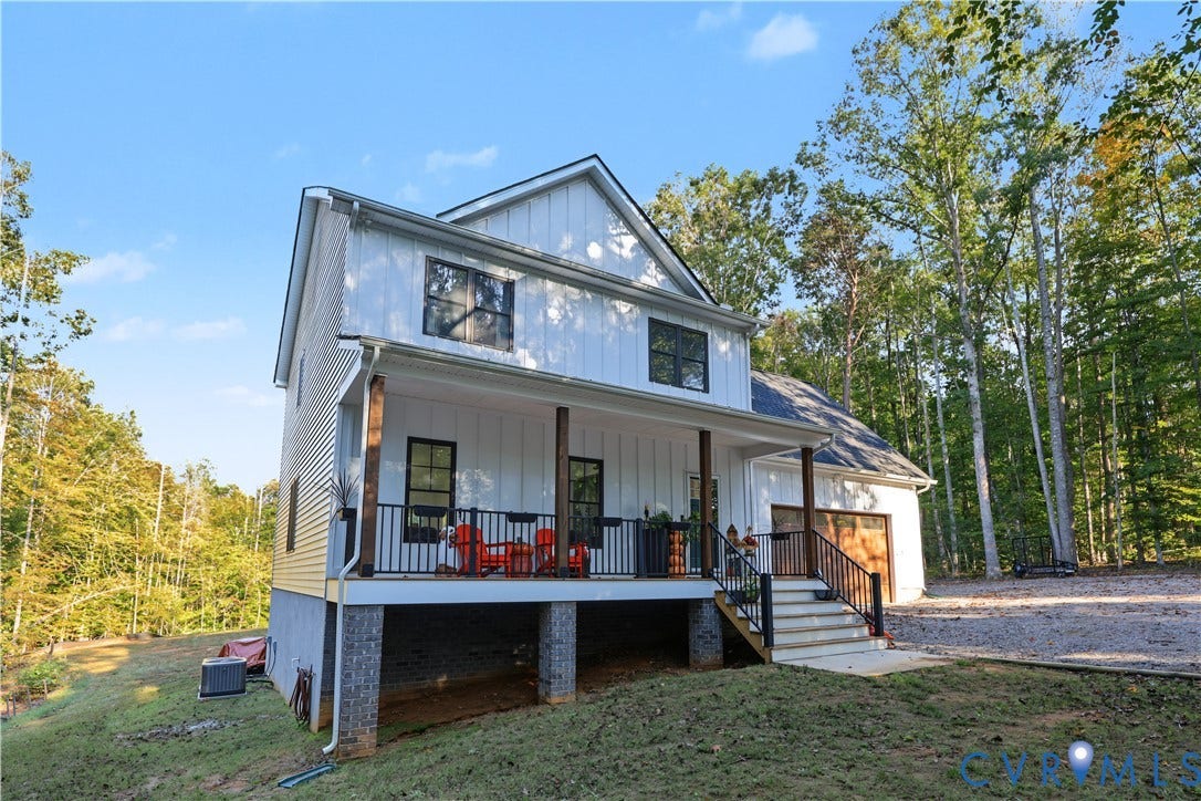 3851 County Line Road, Flemings Mill, Goochland, VA 23084 Two-story residence featuring white board-and-batten siding, a raised covered porch with dark metal railings, wood-wrapped support pillars, and a multi-car garage