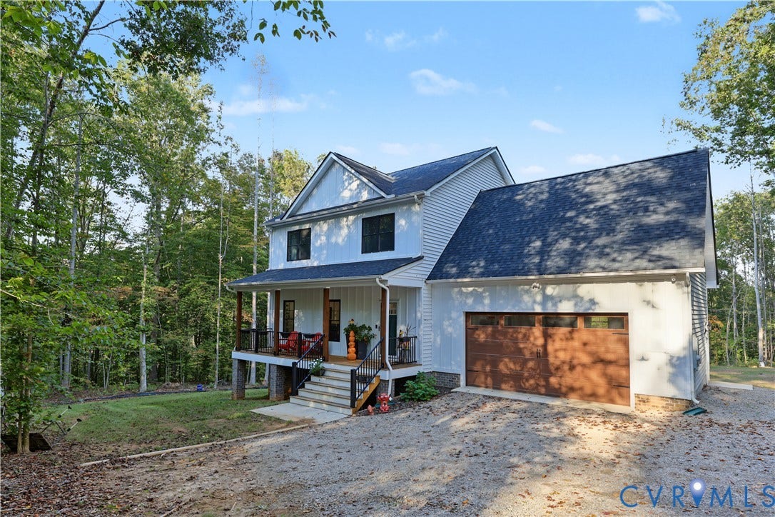 3851 County Line Road, Flemings Mill, Goochland, VA 23084 Two-story home with white vertical and horizontal siding, covered front porch, wood-finished garage door, and stone foundation elements