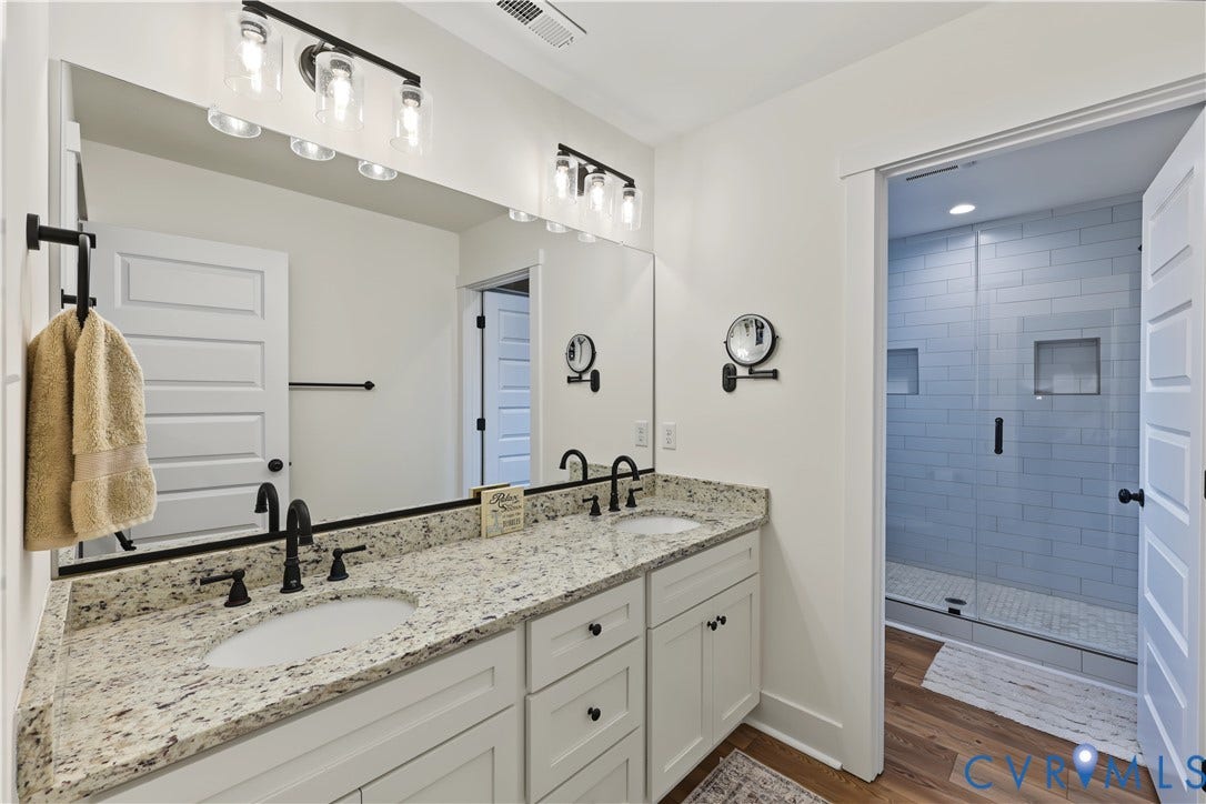 3851 County Line Road, Flemings Mill, Goochland, VA 23084 Double vanity with stone countertop, undermount sinks, matte black fixtures, large frameless mirror, and shower enclosure with subway tile surround