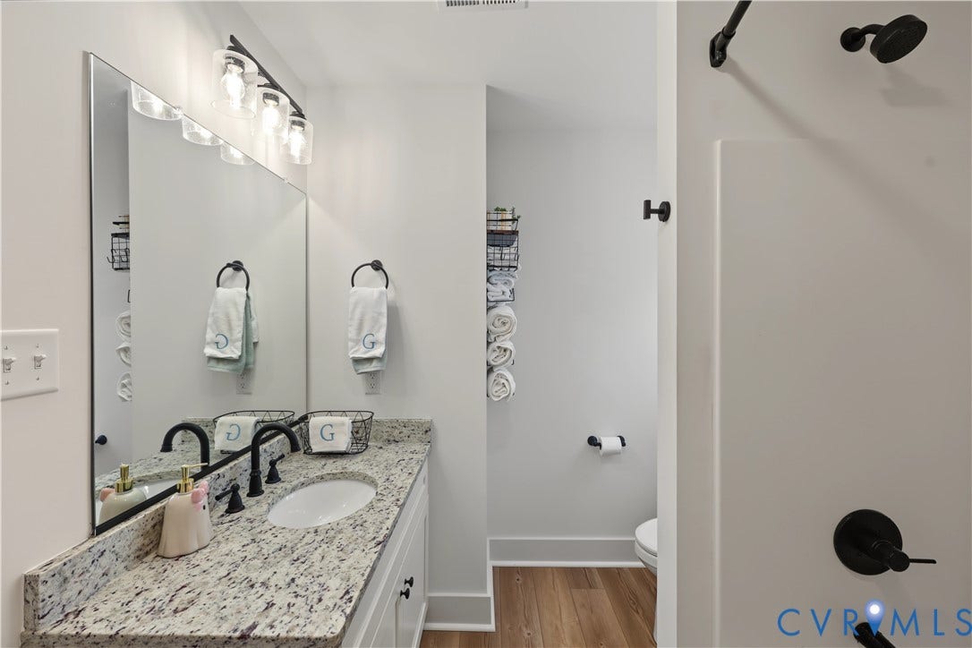 3851 County Line Road, Flemings Mill, Goochland, VA 23084 Vanity featuring a stone countertop with an integrated oval sink, matte black faucet, wall-mounted lighting, and wood-finish flooring
