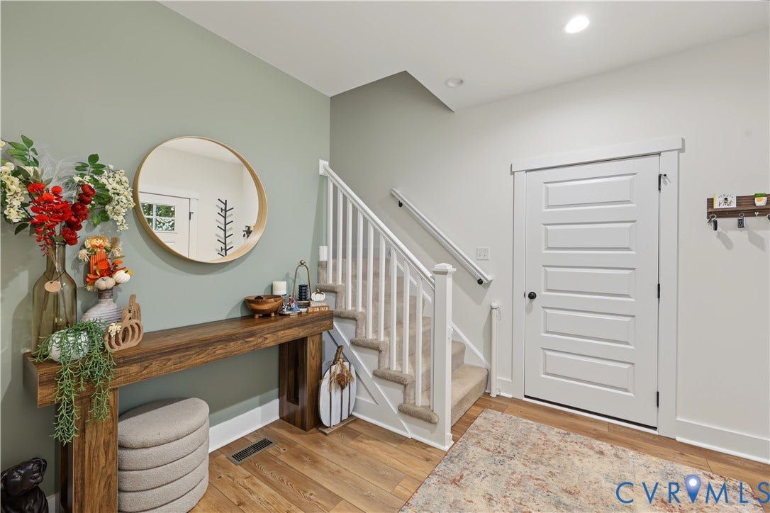 3851 County Line Road, Flemings Mill, Goochland, VA 23084 Entryway featuring a five-panel shaker-style door, wood-finish flooring, and a staircase with white balusters and carpeted treads, accented by a painted sage feature wall