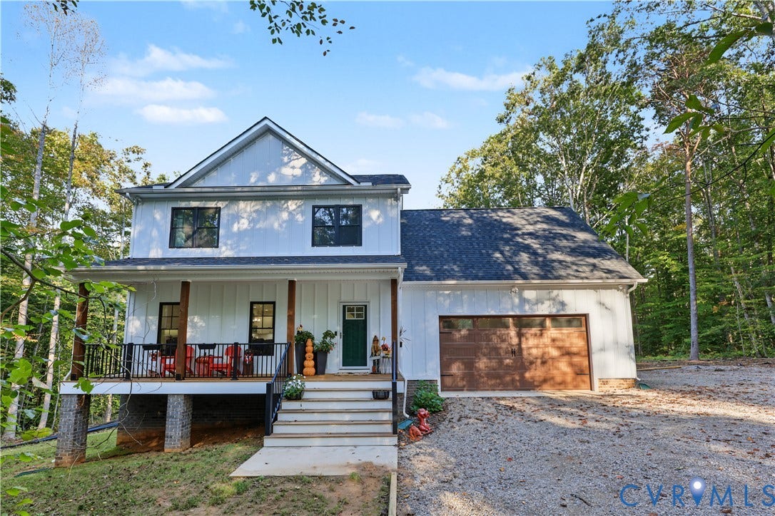 3851 County Line Road, Flemings Mill, Goochland, VA 23084 Two-story residence featuring white board-and-batten siding, a covered front porch with dark metal railings, a stone-accented foundation, and a double-car garage with a wood-finish door