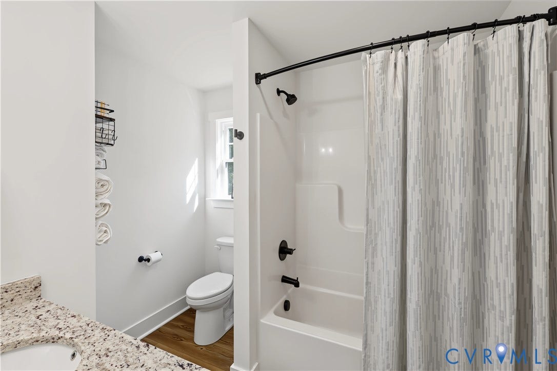 3851 County Line Road, Flemings Mill, Goochland, VA 23084 Bathroom featuring a composite tub surround with matte black plumbing fixtures, wood-finish flooring, and a stone-surface vanity countertop
