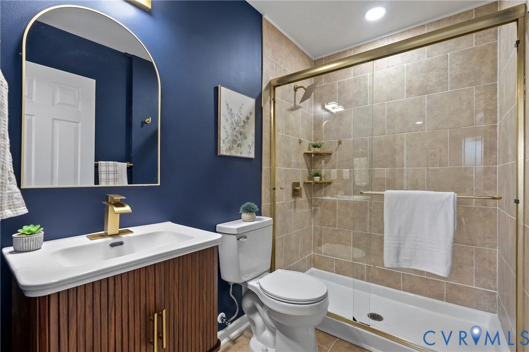 3207 Winchester Street, Henrico, VA 23231 Bathroom featuring a ribbed wood-finish vanity, arched gold-framed wall mirror, gold-toned faucet, and a walk-in shower with tiled surround and gold-toned frame