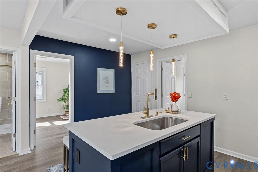 3207 Winchester Street, Henrico, VA 23231 Kitchen island featuring a white countertop, undermount stainless steel sink, brass-finish faucet, and navy blue cabinetry with metallic hardware, accented by three suspended cylindrical pendant lights