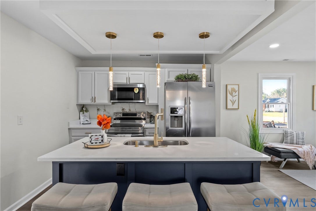 3207 Winchester Street, Henrico, VA 23231 Kitchen featuring a central island with a solid-surface countertop and undermount sink, white cabinetry, stainless steel appliances, recessed ceiling detail, and three glass pendant lights