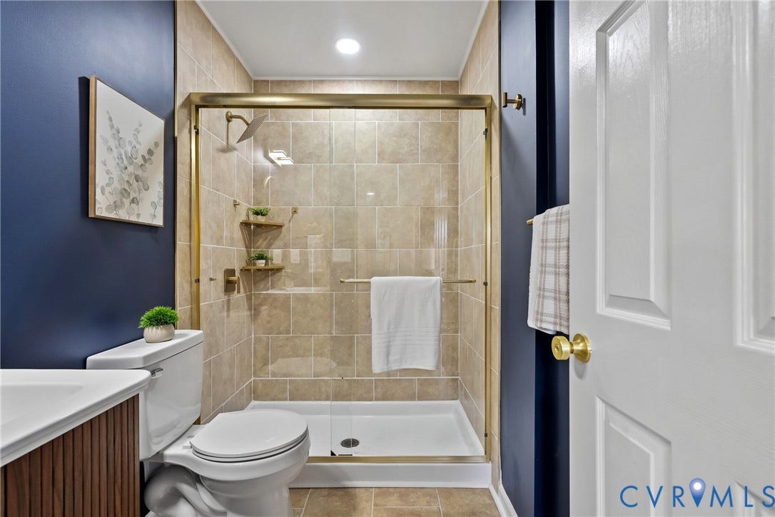 3207 Winchester Street, Henrico, VA 23231 Full bathroom featuring a shower stall with gold-finish frame and fixtures, neutral stone-finish tile surround, built-in shelving, and dark-toned walls