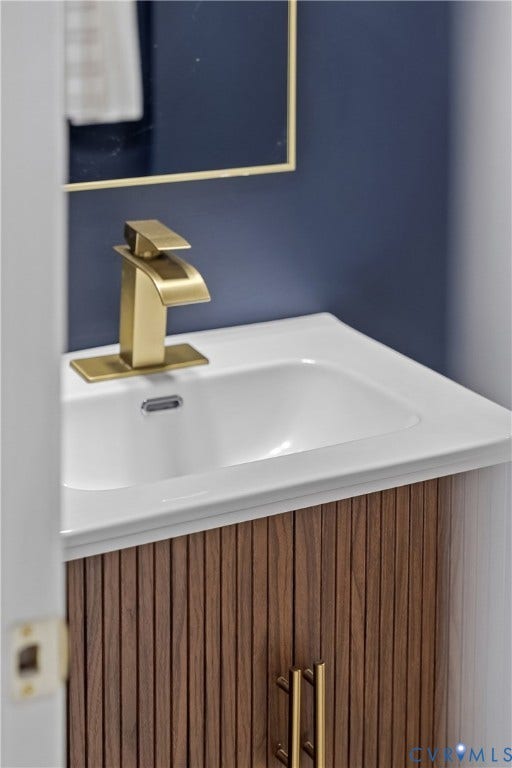 3207 Winchester Street, Henrico, VA 23231 Fluted wood-finish vanity with a white integrated sink, polished gold-tone faucet, matching cabinet hardware, and gold-trimmed mirror