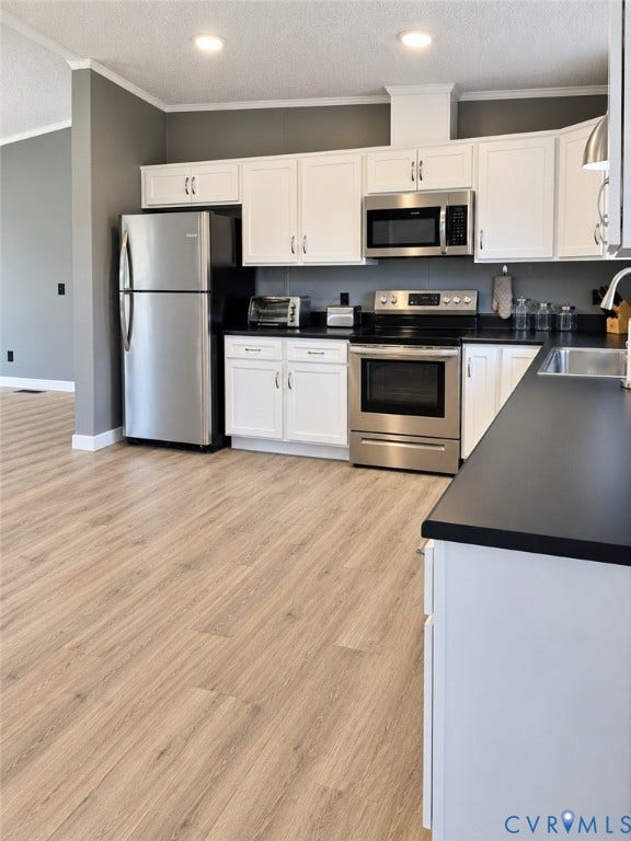 Kitchen featuring white shaker-style cabinetry, stainless steel appliances, dark solid-surface countertops, and wood-finish flooring