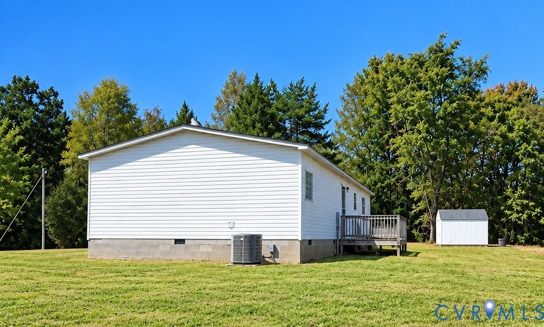 White vinyl siding exterior featuring a block foundation, outdoor wood deck, central air conditioning unit, and a detached storage shed situated on a grass lot