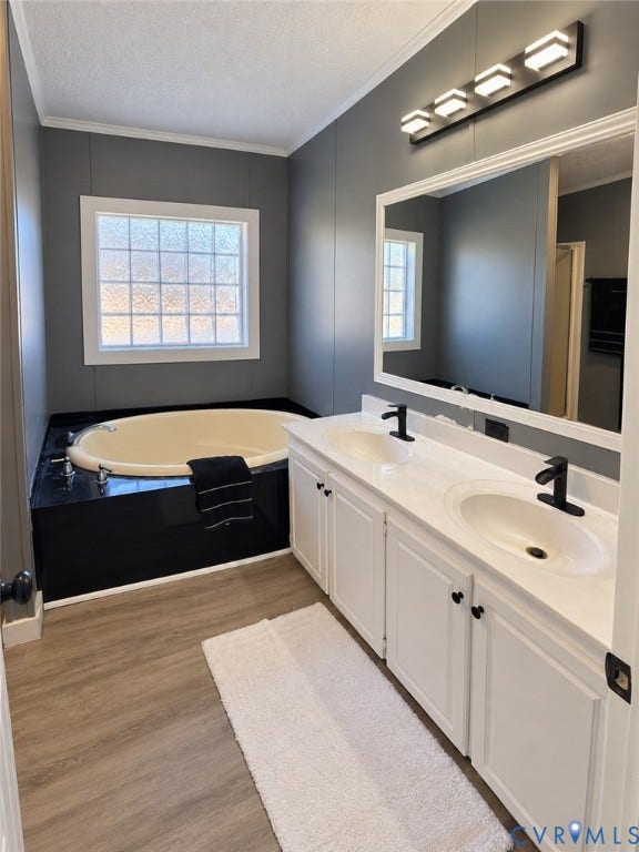 Dual-sink vanity with white cabinetry, light-toned countertop, and matte black fixtures, paired with a deep soaking tub featuring a black surround and wood-finish flooring