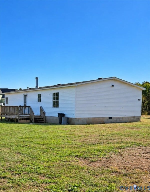 Exterior featuring white vinyl siding, a raised wood deck with integrated stairs, and a concrete block foundation set on a expansive grass lot