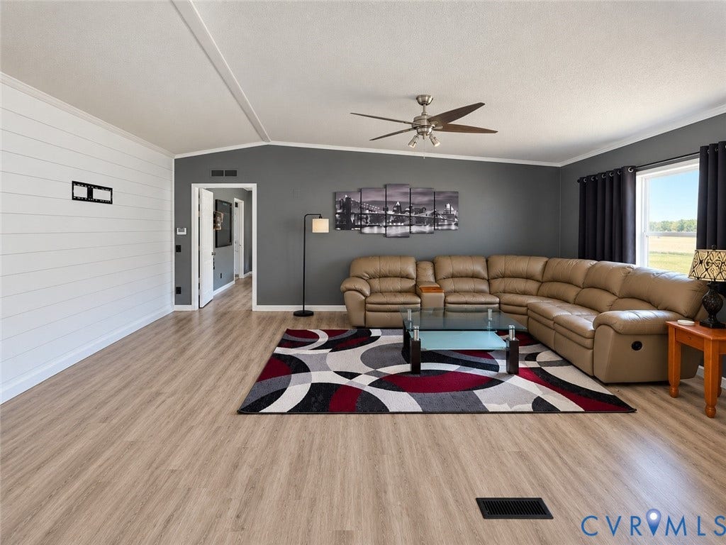 Living area featuring wood-finish flooring, white shiplap accent wall, grey wall paint, and a ceiling-mounted fan with integrated lighting