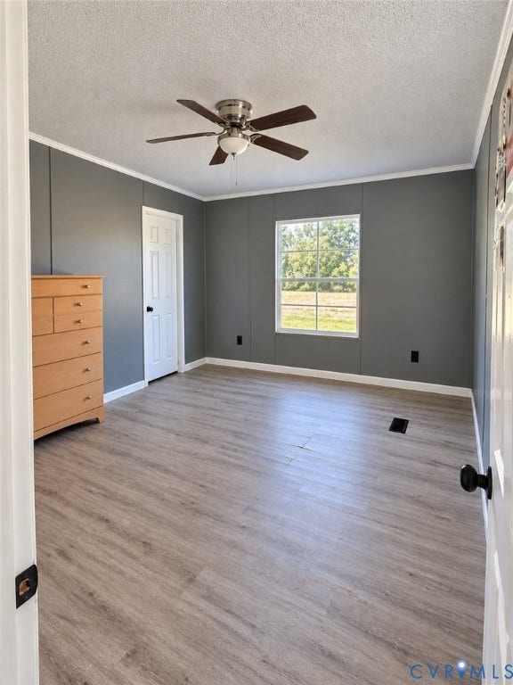 Room featuring wood-finish flooring, dark grey wall panels, a multi-pane window, and a ceiling fan