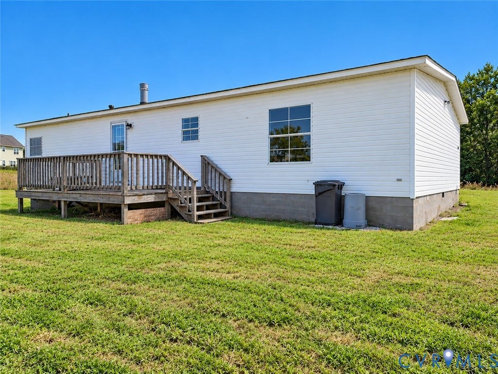 Exterior featuring white horizontal siding, a raised wood deck with staircase, and a concrete block foundation set on an expansive grass lot