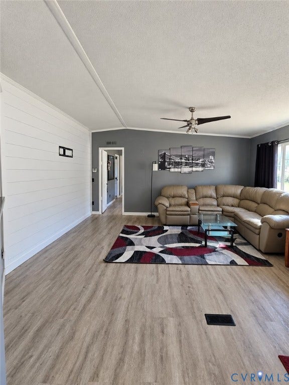 Living area featuring wood-finish flooring, white shiplap accent wall, and a multi-blade ceiling fan with integrated lighting