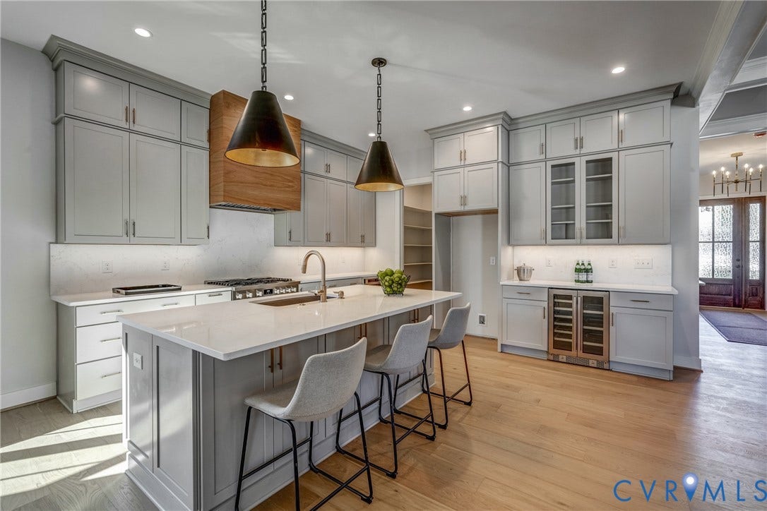 12101 Blunt's Bridge Estates Court, Blunt's Bridge Estates, Doswell, VA 23047 Kitchen featuring shaker-style cabinetry, an oversized quartz-topped island, wood-finish flooring, a custom wood-paneled range hood, and integrated stainless steel beverage refrigeration