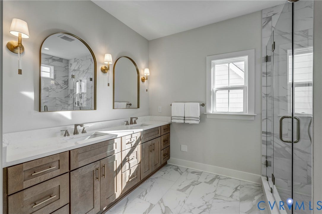 12101 Blunt's Bridge Estates Court, Blunt's Bridge Estates, Doswell, VA 23047 Double vanity with wooden cabinetry and stone countertop, dual arched wall mirrors, wall-mounted brass light fixtures, glass-enclosed shower with tiled surround, and large-format tile flooring