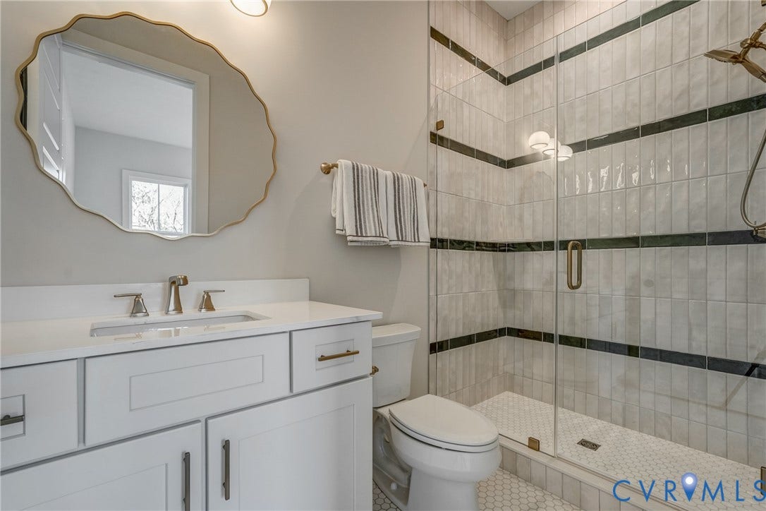 12101 Blunt's Bridge Estates Court, Blunt's Bridge Estates, Doswell, VA 23047 Bathroom featuring a white vanity with a solid-surface countertop, an oval wall mirror with scalloped gold-tone trim, a walk-in shower with a glass enclosure, and decorative tile accents