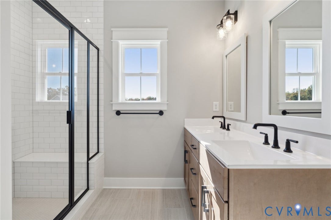 9131 Terroir Lane, Viniterra Villas, New Kent, VA 23124 Double vanity with stone countertop and matte black fixtures, walk-in shower with white subway tile, built-in shower bench, and wood-finish cabinetry