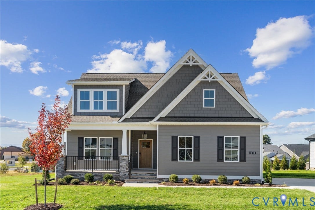 9131 Terroir Lane, Viniterra Villas, New Kent, VA 23124 Two-story residence featuring horizontal and shingle-style siding, a covered front porch with stone-veneer accents, gable roof detailing, and dark-framed shutters