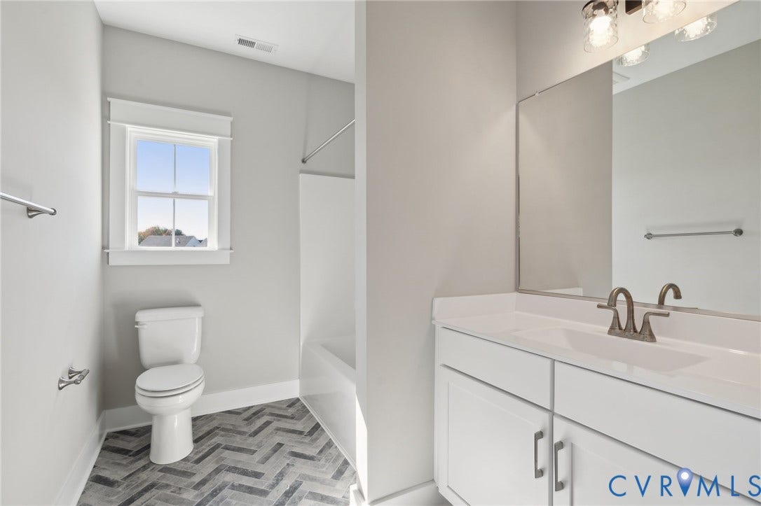 9131 Terroir Lane, Viniterra Villas, New Kent, VA 23124 Bathroom featuring white cabinetry, an integrated vanity top, multi-light fixture, herringbone-patterned flooring, and a window with casing trim