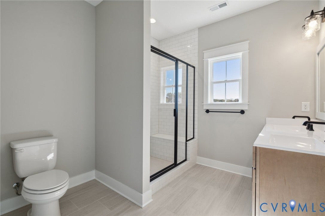 9131 Terroir Lane, Viniterra Villas, New Kent, VA 23124 Walk-in shower with white subway tile surround, glass enclosure with black metal frame, double vanity with solid surface countertop, and wood-finish flooring