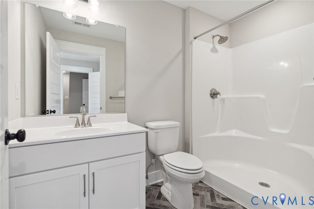 9131 Terroir Lane, Viniterra Villas, New Kent, VA 23124 Bathroom featuring a white vanity cabinet with a stone countertop, integrated sink, oversized wall-mounted mirror, and a tub-shower combination with a surround, complemented by herringbone-pattern flooring