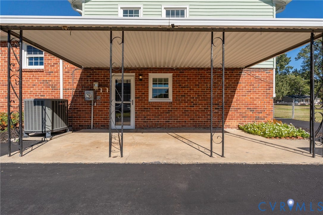 9329 Totopotomoy Trail, Ashland, VA 23005 Covered carport featuring a concrete pad, decorative wrought iron supports, brick exterior cladding, and an asphalt driveway