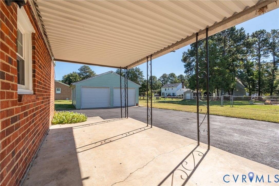 9329 Totopotomoy Trail, Ashland, VA 23005 Covered concrete patio featuring decorative metal support posts, brick exterior, paved driveway, and detached two-car garage