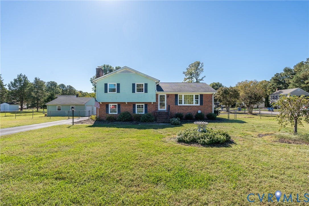 9329 Totopotomoy Trail, Ashland, VA 23005 Split-level exterior featuring a brick and horizontal siding facade, multiple windows with shutters, an attached garage, and an expansive lawn