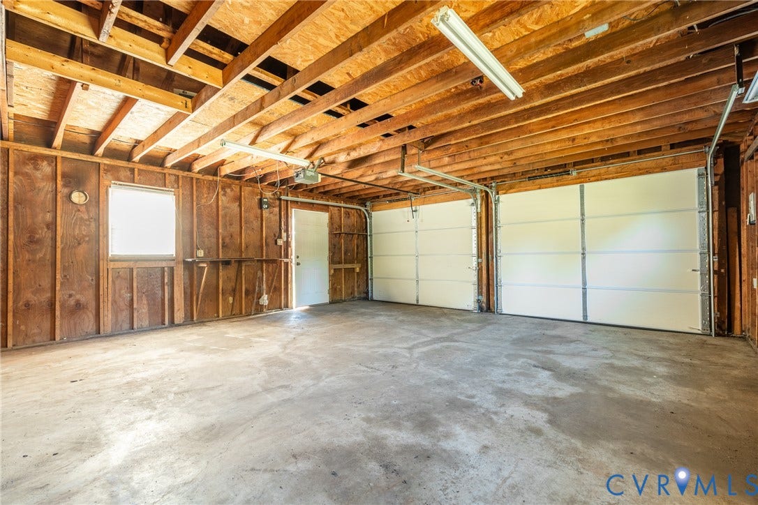 9329 Totopotomoy Trail, Ashland, VA 23005 Two-car garage featuring exposed wood ceiling joists, concrete flooring, dual white sectional garage doors, and a dedicated entry door