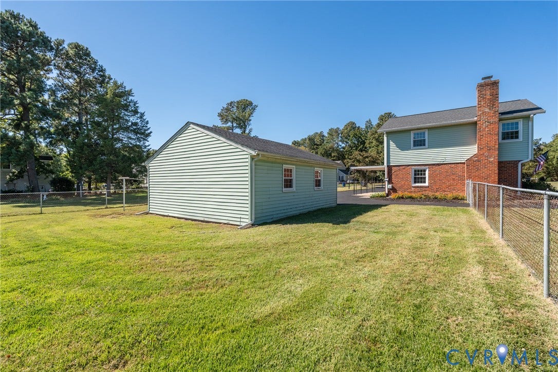 9329 Totopotomoy Trail, Ashland, VA 23005 Exterior featuring a detached garage, brick and vinyl siding, an expansive grassy lot, and chain-link perimeter fencing