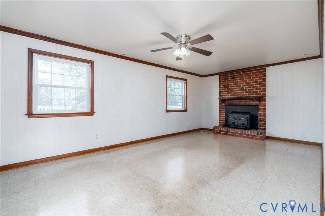 9329 Totopotomoy Trail, Ashland, VA 23005 Brick fireplace featuring a wood-burning insert and mantel, large paneled windows with wood trim, and a ceiling fan with integrated lighting