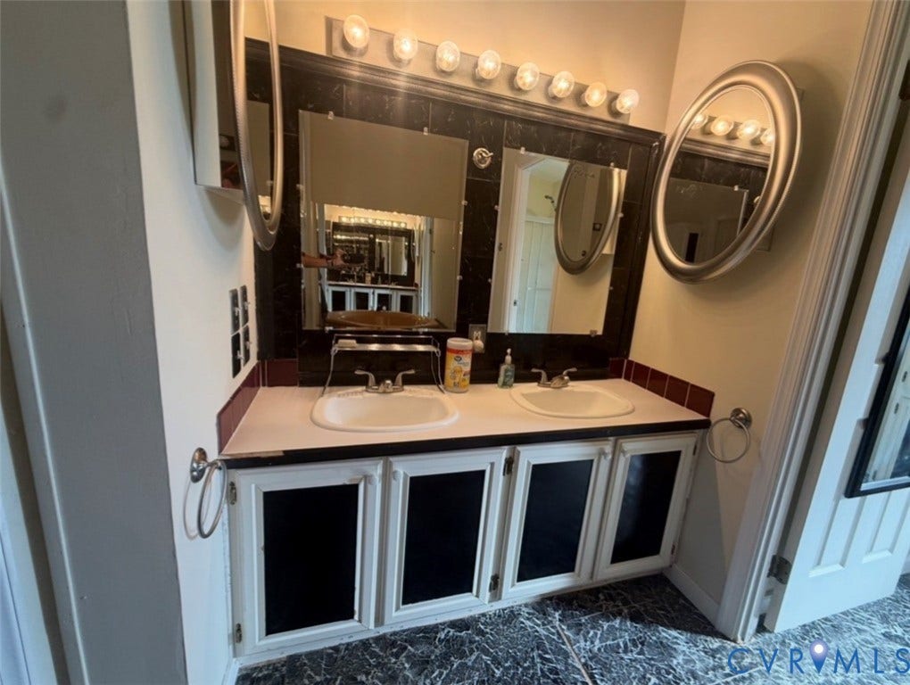26691 Bell Road, Amelia, VA 23002 Dual-sink vanity featuring inset cabinetry with contrasting paneling, integrated mirrors, a polished countertop, and a multi-bulb vanity light fixture