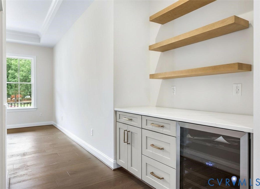 2851 Old Pump Road, Preserve At John Rolfe, Henrico, VA 23233 Built-in cabinetry featuring light-toned shaker-style doors, matte hardware, quartz countertop, integrated wine refrigerator, and floating wood-finish shelving, complemented by wood-finish flooring and crown molding