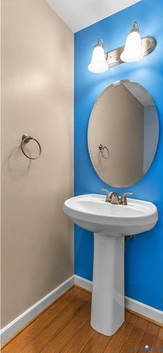 958 Wellston Court, Henrico, VA 23059 Pedestal sink with polished metal dual-handle faucet, oval frameless wall mirror, brushed nickel dual-light fixture, and circular towel ring, accented by wood-finish flooring