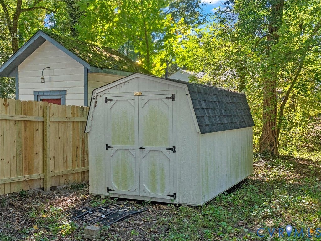 8708 Rainwater Road, Huntingcreek Hills, North Chesterfield, VA 23237 Gable-roof storage structure featuring double-door entry and asphalt shingle roofing, situated within a wooded lot with wood-panel privacy fencing