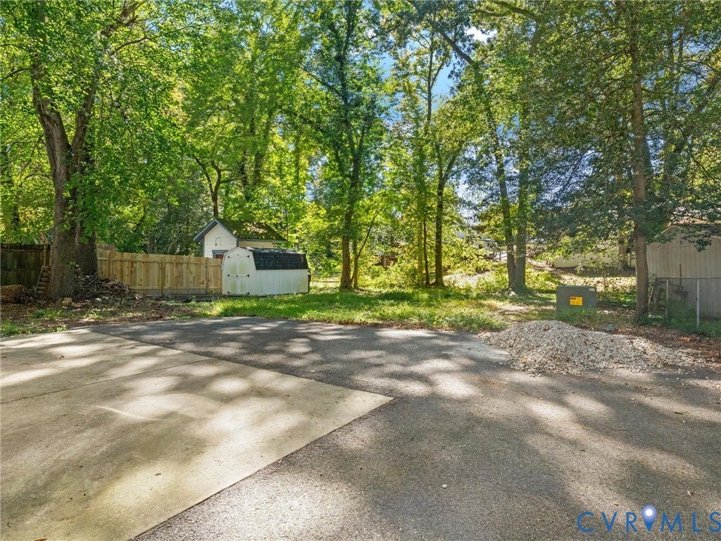 8708 Rainwater Road, Huntingcreek Hills, North Chesterfield, VA 23237 Asphalt and concrete surface, wood privacy fencing, and mature trees on a lot featuring a detached storage structure