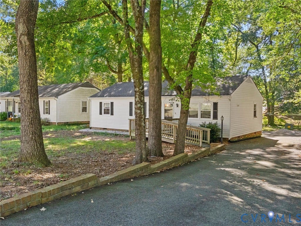 8708 Rainwater Road, Huntingcreek Hills, North Chesterfield, VA 23237 Exterior featuring white siding, a paved driveway, a stepped masonry retaining wall, a wood deck with railings, and mature trees