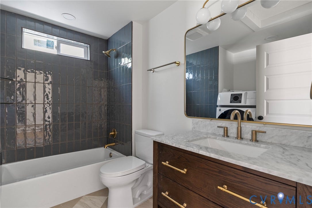 1708 Decatur Street, Swansboro, Richmond, VA 23224 Bathroom featuring a dark wood-finish vanity with a stone countertop, an integrated rectangular sink, gold-tone hardware, a large framed wall mirror, and a tub-shower combination accented by dark vertical wall tiling