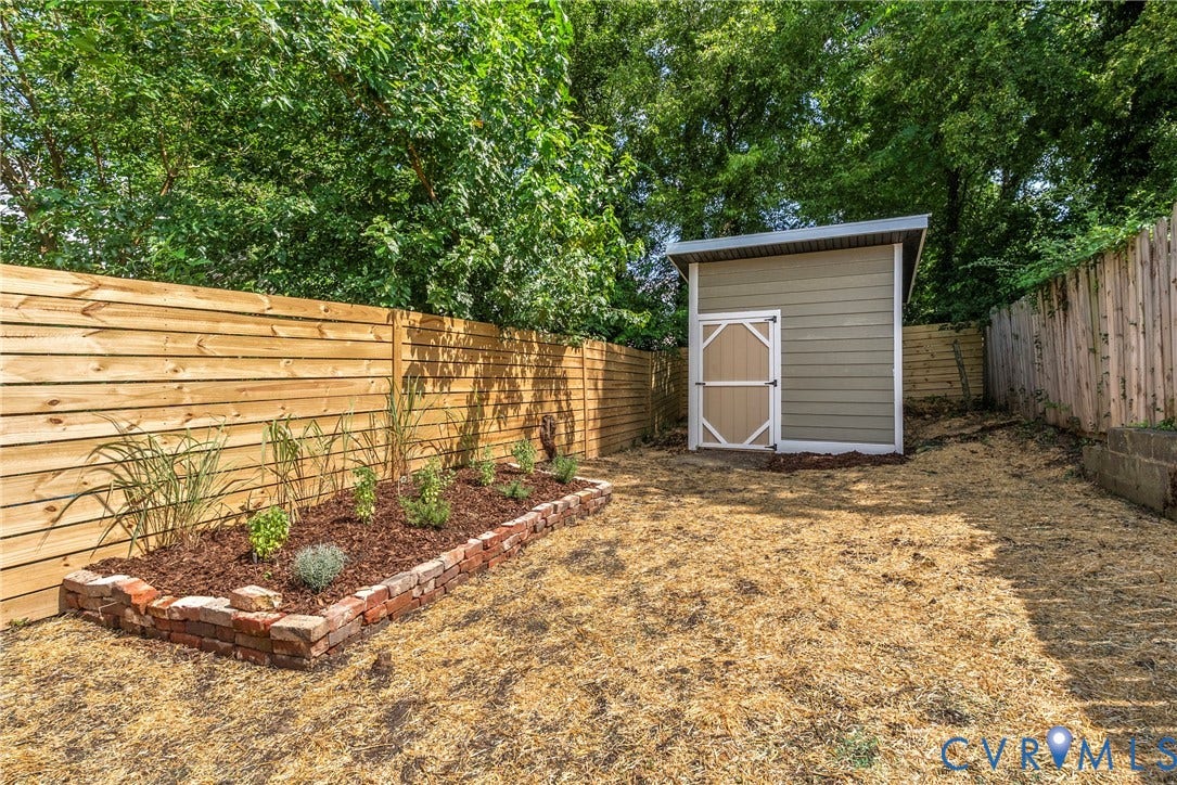 1708 Decatur Street, Swansboro, Richmond, VA 23224 Rear yard featuring a detached storage shed, horizontal wood privacy fencing, and a raised brick-bordered garden bed