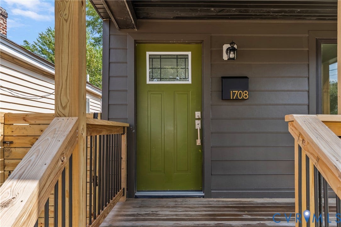 1708 Decatur Street, Swansboro, Richmond, VA 23224 Covered front porch featuring wood-finish decking, dark horizontal siding, a solid entry door with a rectangular window pane, and modern metal railings