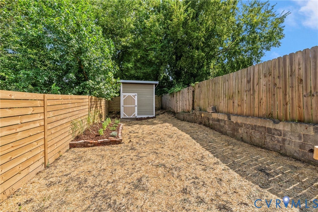 1708 Decatur Street, Swansboro, Richmond, VA 23224 Outdoor area featuring horizontal wood fencing, a masonry retaining wall, a detached storage shed, and a raised garden bed with brick edging