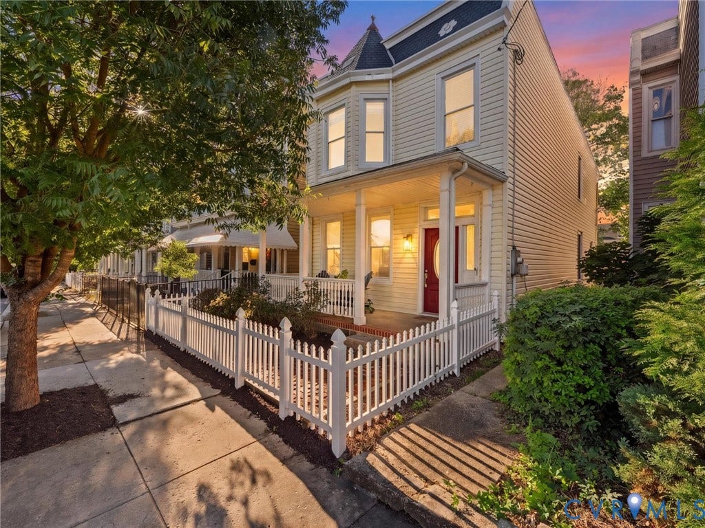 2217 Idlewood Avenue, Byrd Park, Richmond, VA 23220 Victorian-inspired exterior featuring light-toned siding, a covered front porch, a turret, and a white picket fence
