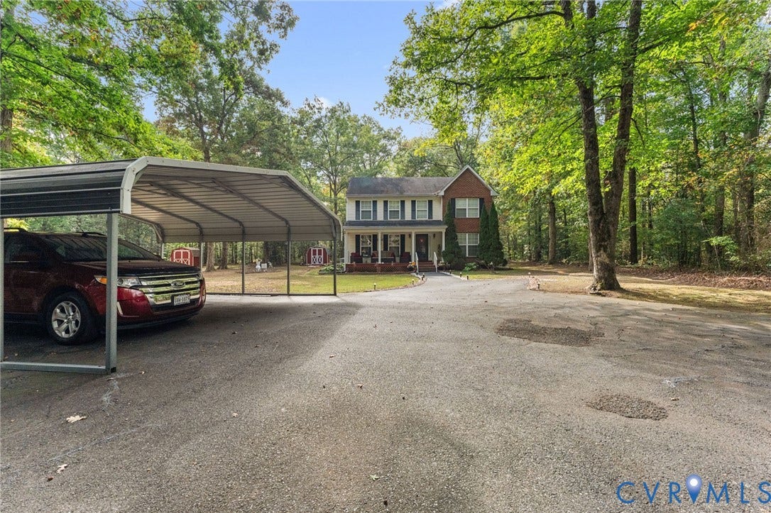 17030 Courtney Road, Reedy Church District, Hanover, VA 23069 Two-story brick exterior home featuring a covered front porch, an attached metal carport, and a gravel driveway situated on a wooded lot