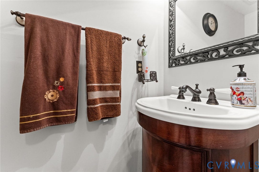 17030 Courtney Road, Reedy Church District, Hanover, VA 23069 Curved wood vanity cabinet with white ceramic basin, dark-finish widespread faucet, and decorative wall-mounted mirror